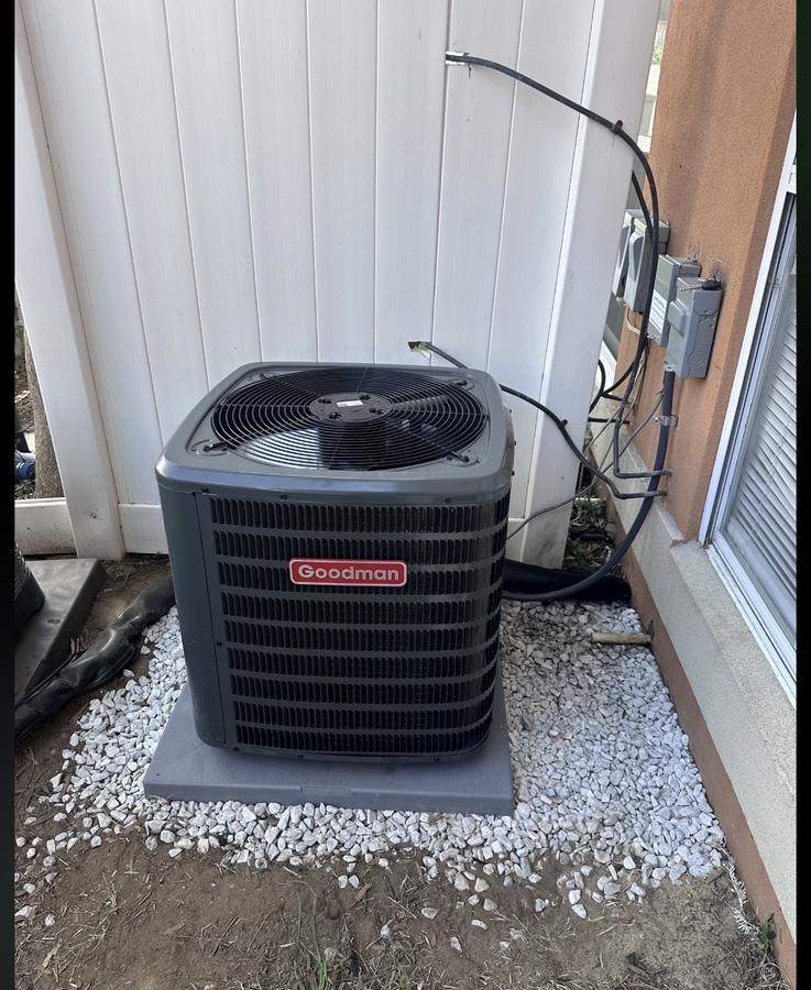 New Goodman air conditioning condenser installed on a level pad with gravel drainage