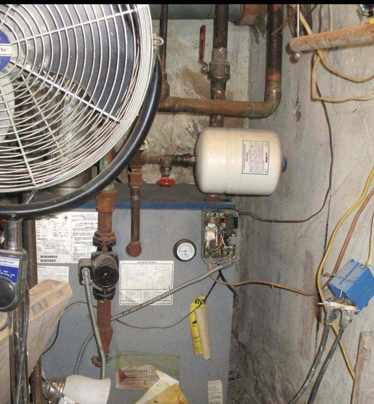 Aging boiler with corroded piping and an old expansion tank in a cluttered basement before replacement