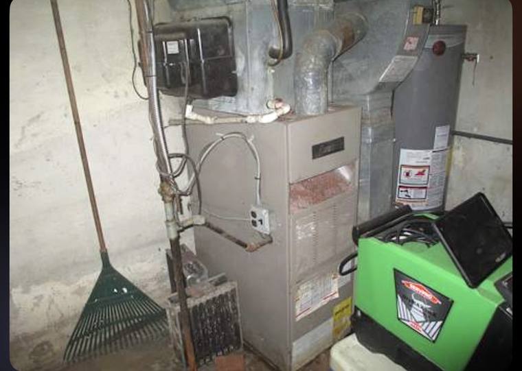 Old furnace with rusted piping in a cramped basement corner before replacement