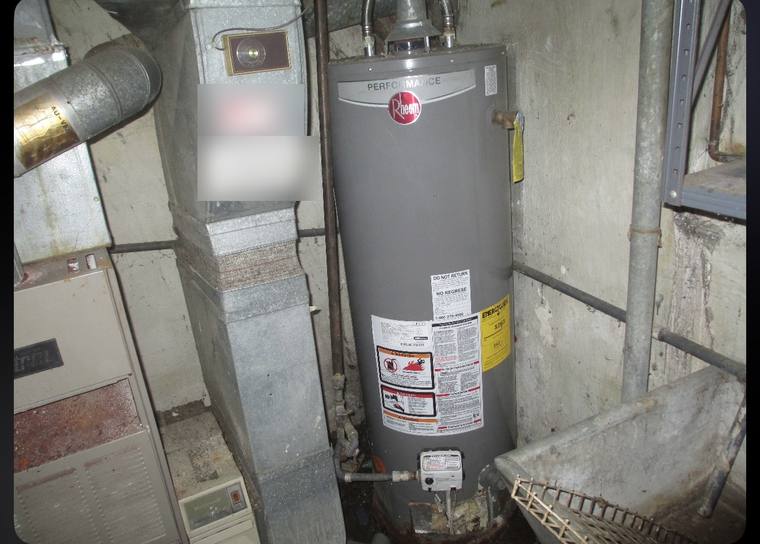Old Rheem gas water heater with a corroded metal flue crammed beside ductwork before replacement