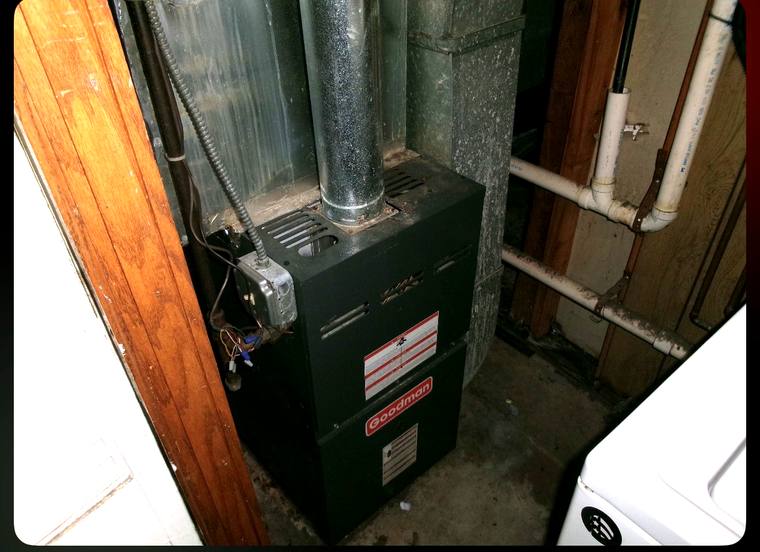 Old furnace with weathered flue pipe and exposed wiring in a cramped basement before replacement