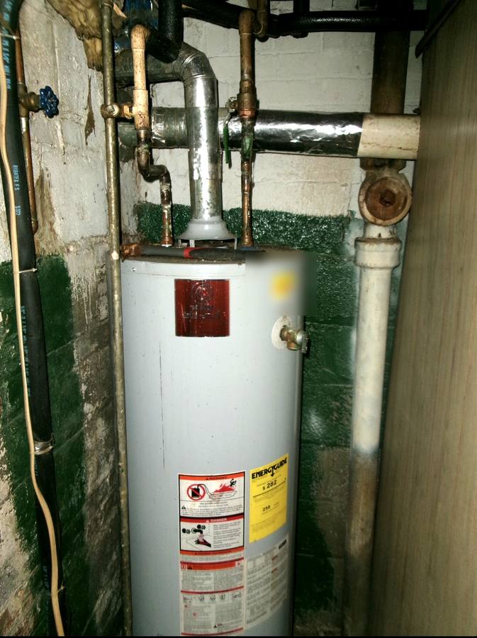 Old gas water heater in a narrow basement closet with aging valves and flue before replacement